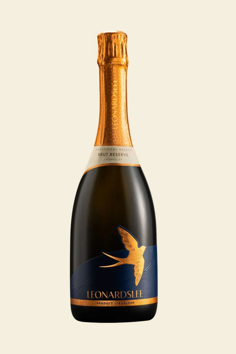 A bottle of Leonard's Life Brut Reserve Champagne with a dark glass body, gold foil on the neck, and a navy blue label featuring a gold swallow design, set against a solid cream background.