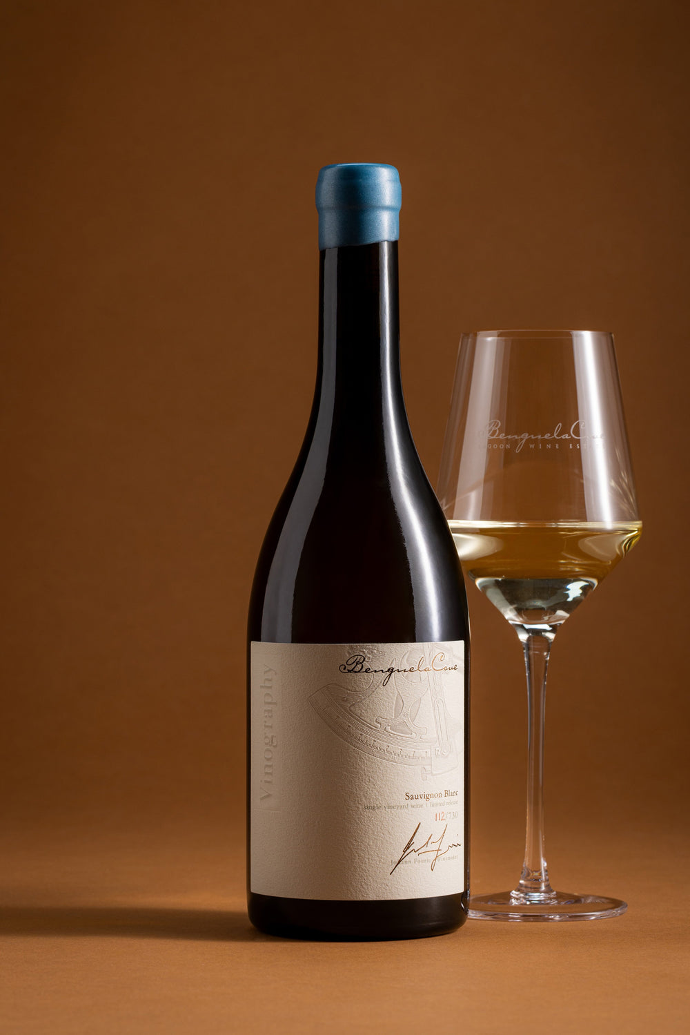 Wine bottle with a blue cap and a glass of white wine on a brown background