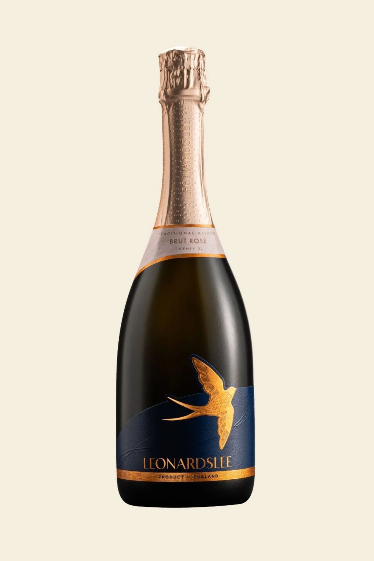 A bottle of Leonard's Lee Champagne Brut Non-Alcoholic with a dark green glass body, a metallic gold foil neck, and a navy blue label featuring a golden swallow in flight, set against a solid cream background.